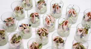 Mehrere Gläser mit einem raffiniert angerichteten Vorspeisensalat, bestehend aus Fischfilets, Kräutern, Beeren und cremiger Basis, auf weißem Untergrund.