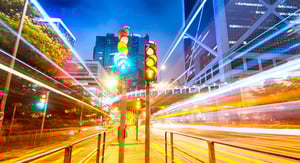 Urban traffic light intersection at night with vehicle light trails and illuminated skyscrapers in the background.
