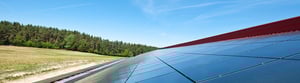 Solaranlage auf einem Schrägdach am Waldrand, mit Blick auf ein offenes Feld und einen klaren blauen Himmel.