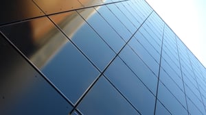 Modern building facade made of dark, reflective metal or glass panels viewed from a low perspective.